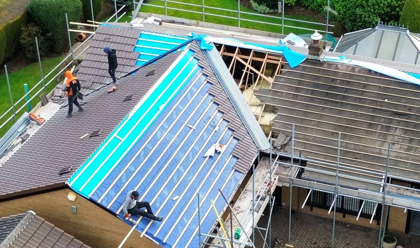 Roofers working on a tiled roof with breathable membrane being laid and scaffolding in place